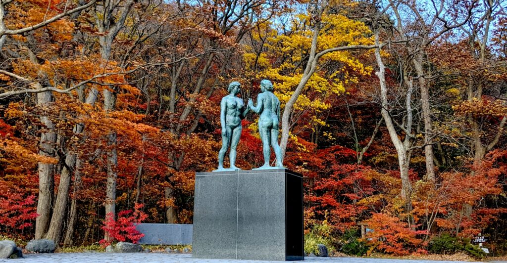 紅葉した木々と十和田湖畔に立つ乙女の像